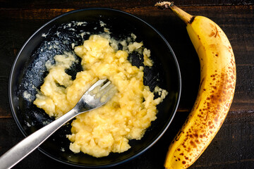 Mashing a Ripe Banana with a Fork: A bowl of mashed banana with a whole banana next to it