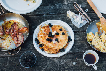 high angle view of camping tabletop with pancakes, bacon, scrambled eggs