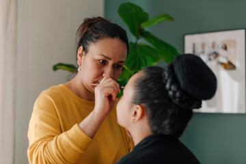 Mother is applying eyeliner on her pre-teen daughter eyes at home