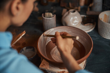 Beautiful young craft woman during process manufacturing clay tableware in pottery workshop