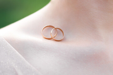 Two gold wedding rings lying on the open shoulder of a young bride in a wedding dress. Wedding...