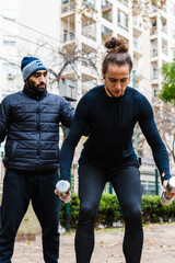 young Brazilian long-haired man being corrected by his Argentinean Latino personal trainer, working out outside