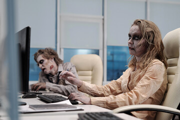 Ugly zombie female sitting in armchair in front of computer monitor