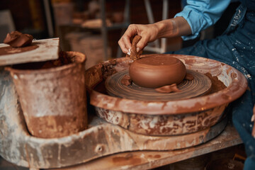 Unrecognized female ceramicist wearing apron working with earthenware materials on special equipments in art studio