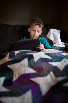 Sick boy blows nose with tissue on couch with tablet and tissues