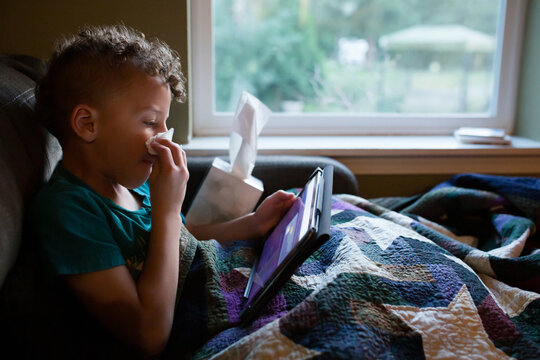 Sick child with tablet wipes nose with tissue 