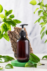 Organic cosmetic product in a brown dispenser on a background of green leaves and tree bark. Eco friendly product.