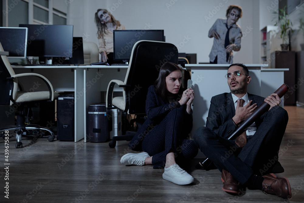 Poster two terrified managers waiting for zombies on the floor in office