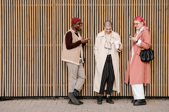 Cheerful diverse friends using smartphones and chatting on street