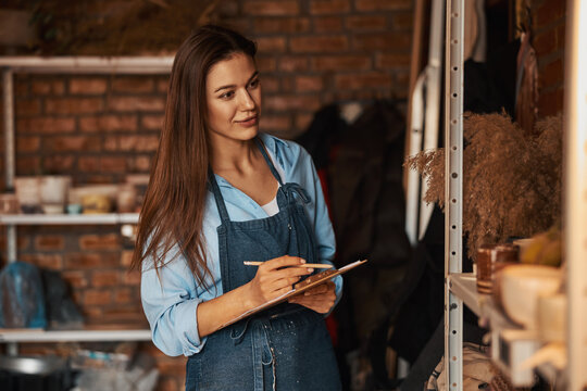 Beautiful elegant craft woman with long hair holding clipboard in hands in art modern studio