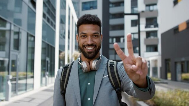 Cheerful young man gesturing V sign with fingers outdoors in city, covid-19 vaccination campaign concept.