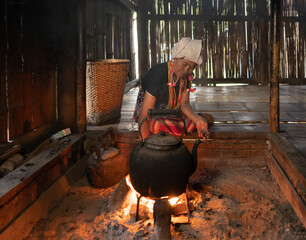 A portrait of karen tribe woman boiling water by using traditional kettle and fire, water heater at...