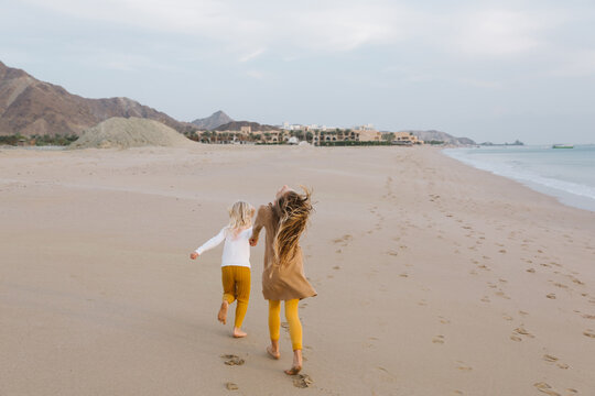 Two girls running on the beach in warm clothes