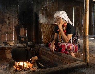 A portrait of karen tribe woman using cigarette to smoke, boiling water by using traditional kettle...