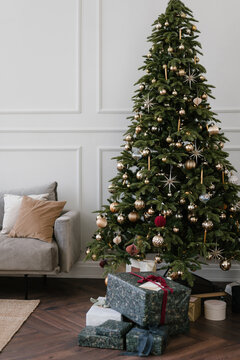 Christmas tree with presents placed near couch in cozy apartment