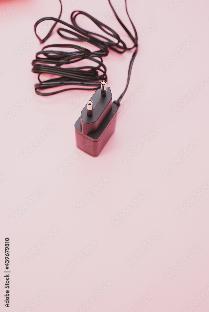 Wall mural Vertical shot of wired charger adapter isolated on pink background