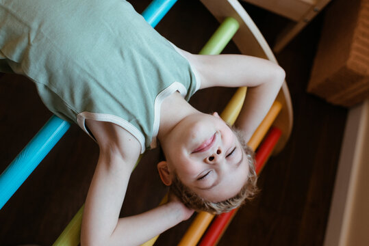 Blond child resting on a rainbow pikler in his room