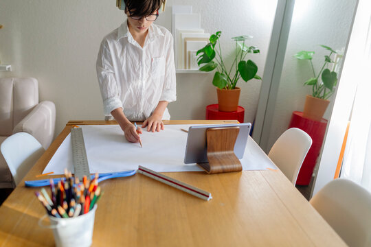 Pre-teen Boy wearing headphones drawing a map on big paper on a table with a device