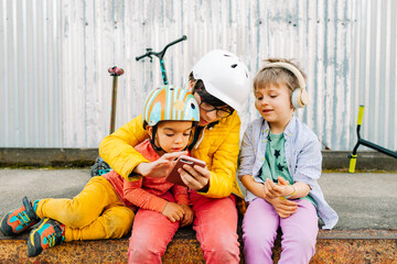 kids sitting by a rustic wall while using a phone