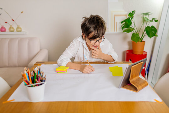 Smiling Pre-teen Boy drawing on paper while having a conference with tablet