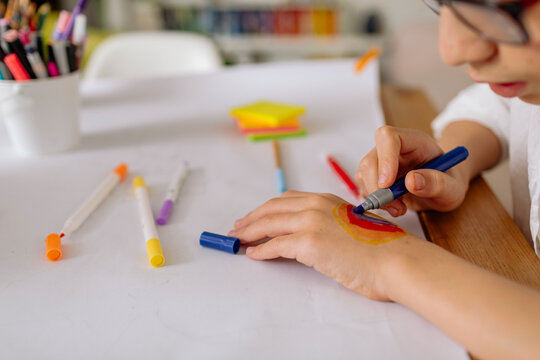 Cropped view of pre-teen boy drawing on his hand a rainbow with markers