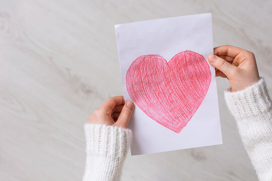Close-up of a child's hand with a red heart drawn on white paper on a wooden background. Mother's Day. The child's love for his mother. Copy space for text.