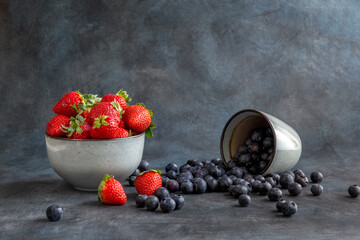 Strawberries and blueberries in a cup. Blueberries are scattered on the table. Blurred background. Rustic style. Healthy diet. High quality photo