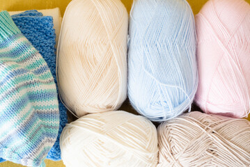Fototapeta na wymiar Balls of woolen threads, knitting needles and knitted clothes on the yellow sofa top view background.