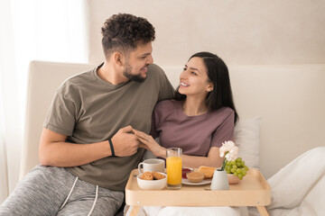 Obraz na płótnie Canvas Cheerful married couple enjoying breakfast and honeymoon in hotel bedroom