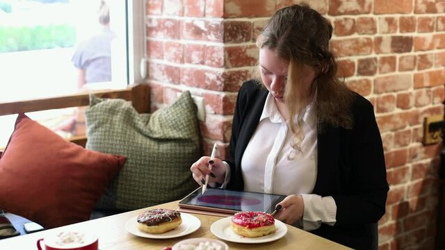 Girl in a cafe makes a sketch on an electronic tablet.
