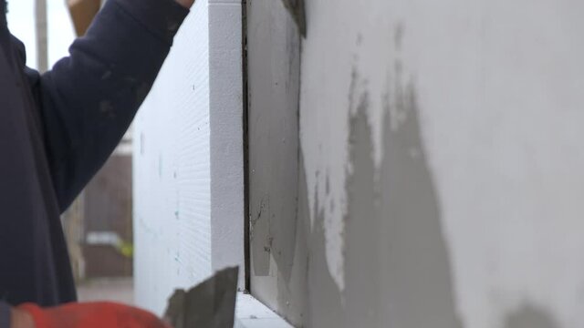 Construction worker covering house wall with adhesive cement glue berore installing styrofoam insulation sheets for thermal protection.