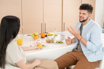 Young couple talking by breakfast while sitting by kitchen table