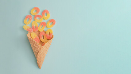 Creative summer food idea with colorful gummy candies in an ice cream cone. Bright blue background,...