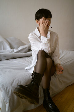Young woman sits on a bed and smoking