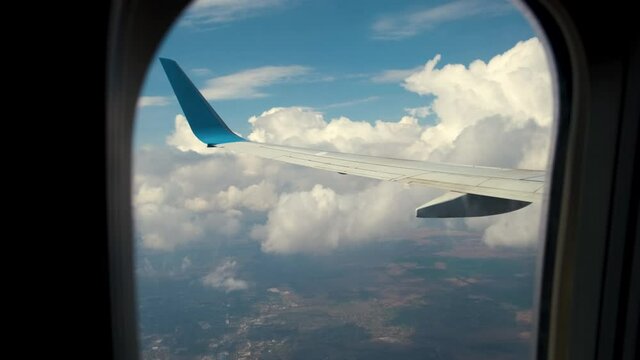 View of jet airplane wing from inside flying through white puffy clouds in blue sky. Travel and air transportation concept.