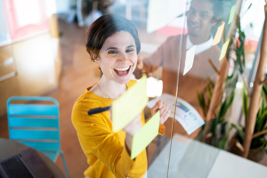 Businesswoman Putting Post-It Notes On Glass Board