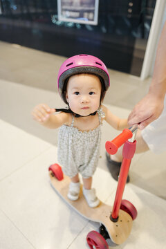 Asian babygirl wearing a helmet and playing a scooter under the protection of her father