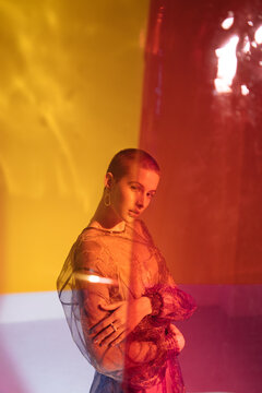 Bald woman in elegant dress in studio with light effects