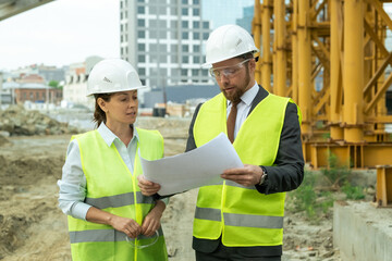 Young female engineer listening to colleague explaining sketch on blueprint