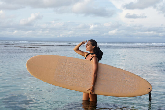 Girl in with a surfboard looks at the ocean and waves. Surfer girl