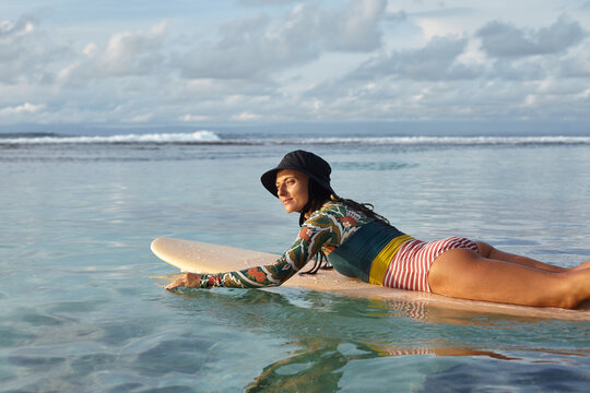A girl in a panama hat lies on the surf and rowing in the ocean. Surfer girl