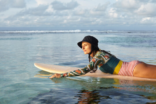 A girl in a panama hat lies on the surf and rowing in the ocean. Surfer girl