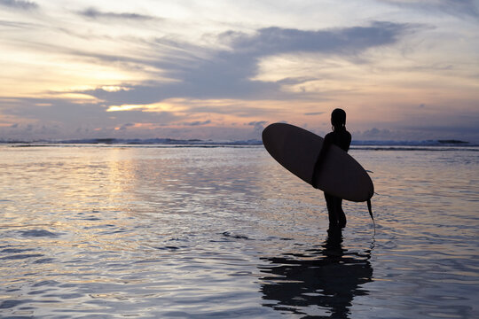 Silhouette of a girl with a surf at sunset by the ocean. Surfer girl