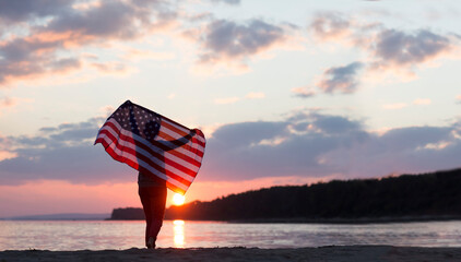 a woman with an American flag on the ocean at sunset. Independence Day. The United States...