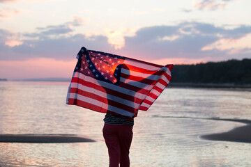 a woman with an American flag on the ocean at sunset. Independence Day. The United States...