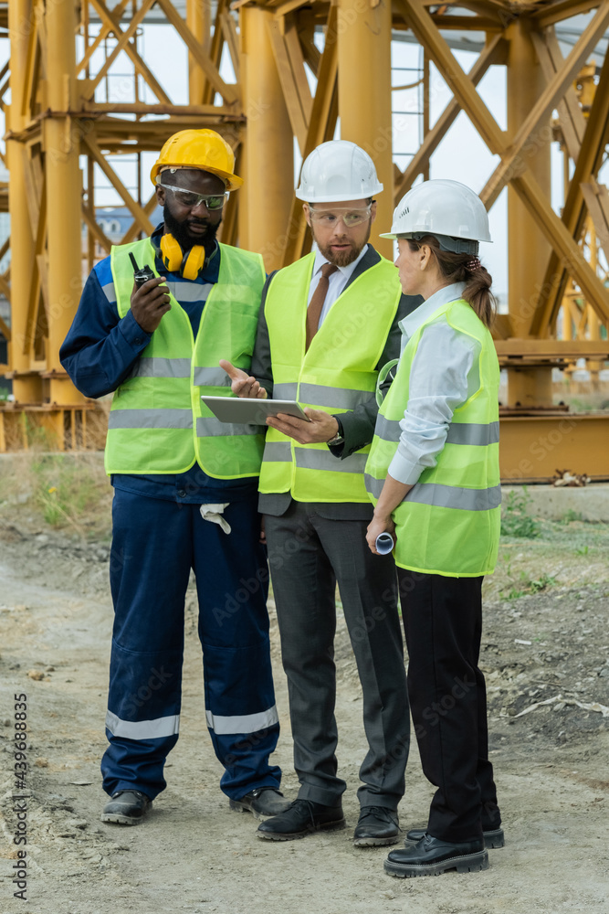 Poster Group of builders discussing sketch on tablet screen at construction site