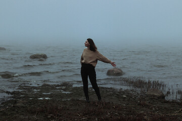 young female stands on a near by foggy sea