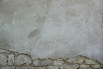 Old stone wall covered with cement. Half of cement on this wall is crumbled. There are cinderblocks under the cement.
