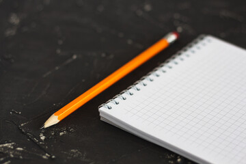 Notepad with a pencil on a dark background. White notepad. Yellow pencil. Dark background. 