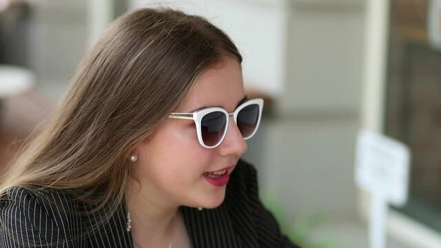 A girl in sunglasses is talking to a friend. Close-up